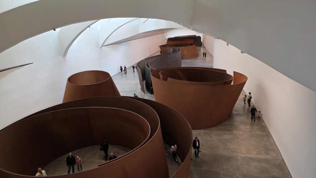 Richard Serra „Az idő kérdése” című installációja a bilbaói Guggenheim Múzeum Bilbao egyik legismertebb alkotása, ahol a monumentális, ívelt acélszobrok a tér, a mozgás és az idő érzékelését formálják át a látogatók számára.